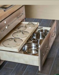 an open drawer in a kitchen with pots and pans on the bottom shelf,