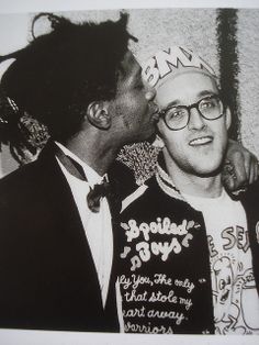 two men are standing next to each other in front of a wall with graffiti on it