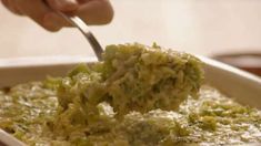 a person scooping broccoli out of a casserole dish with a spoon