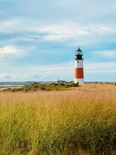 a light house sitting on top of a lush green field next to a tall grass covered field