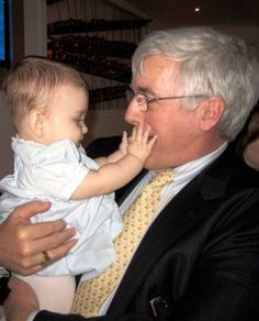 an older man holding a baby in his lap while wearing a tie and suit jacket