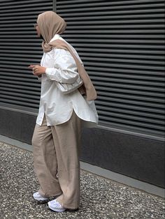 a woman is standing on the sidewalk looking at her cell phone while wearing a hijab