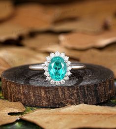 an emerald colored ring sits on top of a piece of wood with leaves around it