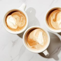 three cups of coffee on a marble table with spoons next to it and another cup in the foreground