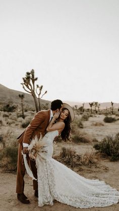 a bride and groom kissing in the desert with cacti on the ground behind them