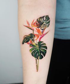 a woman's arm with a colorful flower and leaves tattoo on the left forearm