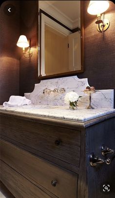 a bathroom with a marble counter top and wooden drawers, along with two lights on either side of the vanity