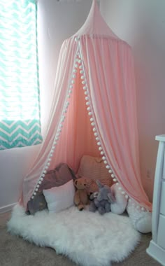 a pink tent with white pom poms and stuffed animals in it, next to a window