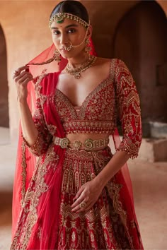 a woman in a red and gold bridal outfit with her hands on her hip