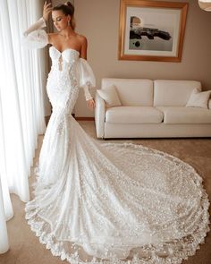 a woman in a white wedding dress standing next to a couch with her arms behind her head