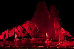 the stage is lit up with red lights and candles in front of large rock formations