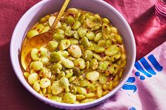 a white bowl filled with green beans on top of a pink table cloth next to a wooden spoon