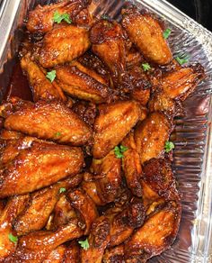 chicken wings with brown sauce and parsley in a glass dish on top of a table