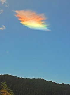 a rainbow colored cloud is in the sky above some trees and grass on a sunny day