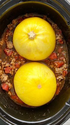 two yellow tomatoes in a slow cooker filled with meat and vegetables, ready to be cooked