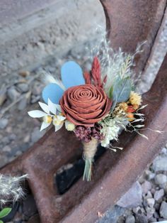 a boutonniere with dried flowers and feathers on an old rusted piece of metal