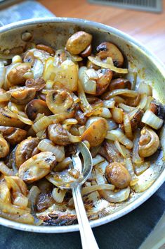 a skillet filled with onions and mushrooms on top of a table next to a spoon