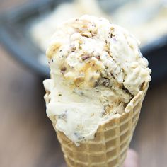 a hand holding an ice cream cone in front of a pan of desserts on a table