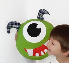 a young boy holding up a green monster pillow to the side of his face,