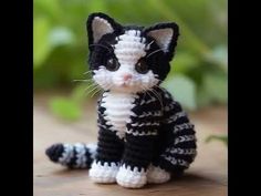 a crocheted black and white cat sitting on top of a wooden table next to green plants