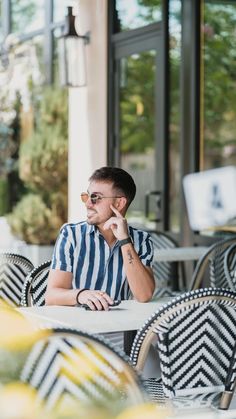 a man sitting at an outdoor table talking on his cell phone while wearing sunglasses and a striped shirt