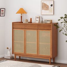 a wooden cabinet with wicker doors in a room next to a lamp and pictures on the wall