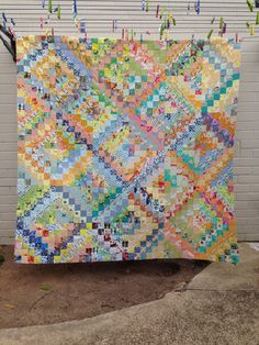 a colorful quilt hanging on a clothesline next to a white brick wall with pegs