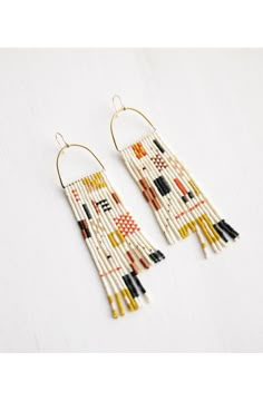 two pairs of earrings with fringes hanging from the side on a white tablecloth