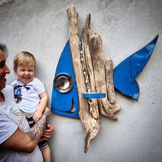 a man holding a child in front of a fish shaped wall hanging on the side of a building