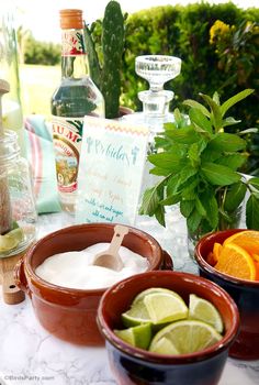 there are three bowls with limes and oranges on the table next to bottles