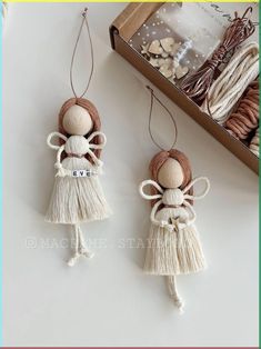 two wooden angel ornaments hanging from strings on a white table next to a box of yarn