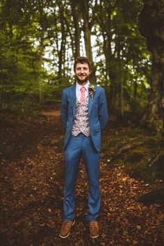 a man wearing a blue suit and tie standing in the woods