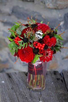 a vase filled with lots of red flowers on top of a wooden table next to a stone wall