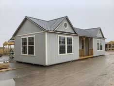 a gray house sitting in the middle of a parking lot next to other houses and construction materials