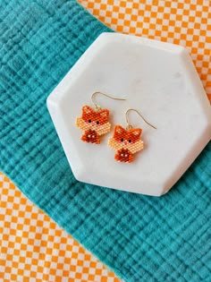 a pair of beaded fox earrings sitting on top of a blue and orange towel