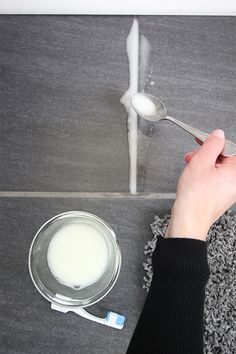 a person is using a spoon to paint a tile floor with white paint on it