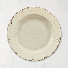 an empty white plate with brown speckles on the rim sits on a marble surface