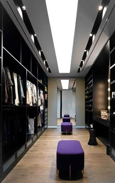 a walk - in closet with purple foot stools and clothes on shelves, lighting up the room