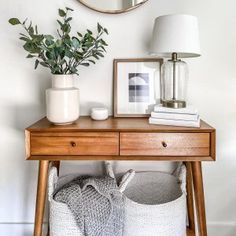 a wooden table with two baskets and a mirror on it, next to a plant