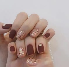 a woman's hand with some brown and gold nail polishes on her nails