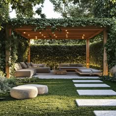 an outdoor living area with grass, rocks and plants on the ground in front of a wooden pergoline