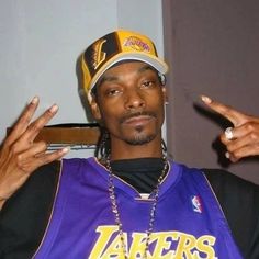 a man in a lakers jersey pointing to the side with his fingers up and wearing a hat