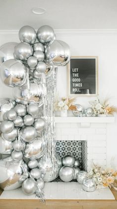 silver balloons are stacked on top of each other in front of a fireplace with flowers