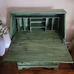 an old green wooden desk with drawers on it's sides and flowers in vases next to it