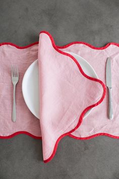 a white plate with a fork and knife next to a pink napkin on a gray surface