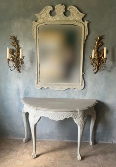 a white table with a mirror on the wall and two candle holders next to it