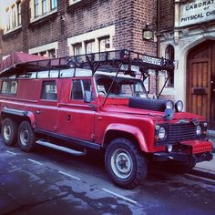 an old red land rover parked on the side of the road in front of a brick building