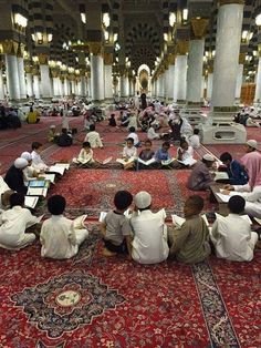 many people are sitting on the floor in a large room with red carpet and white pillars