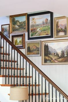 there are many pictures on the wall above the bannister and below the stairs