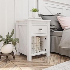 a white bedside table next to a bed with a plant on it and other furniture in the background